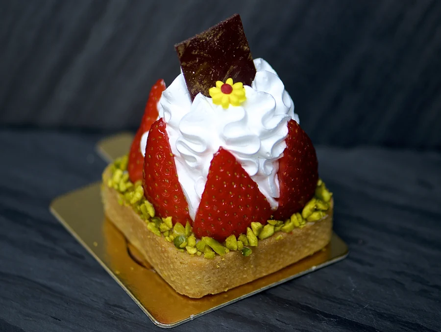 A strawberry-colored L’Artisane pastry with white piped decoration and small flowers